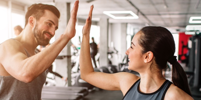 Berufshaftpflicht für Fitnesstrainer Ein Mann und eine Frau klatschen sich im Fitnessstudio ab